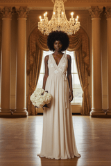 A woman stands in a grand hall wearing a sleeveless cream wedding gown with lace detailing on the bodice and a flowing skirt, holding a large white bouquet. The room features tall columns, draped curtains, a chandelier, and a polished wood floor.