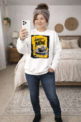 Person wearing a white sweatshirt with a coffee graphic and text, standing in a bedroom.