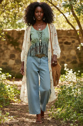 Woman wearing a green lace-up top with fringe details and blue jeans against a gray background