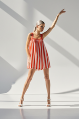 Woman in a red and white striped dress standing on a white staircase with light casting shadows.