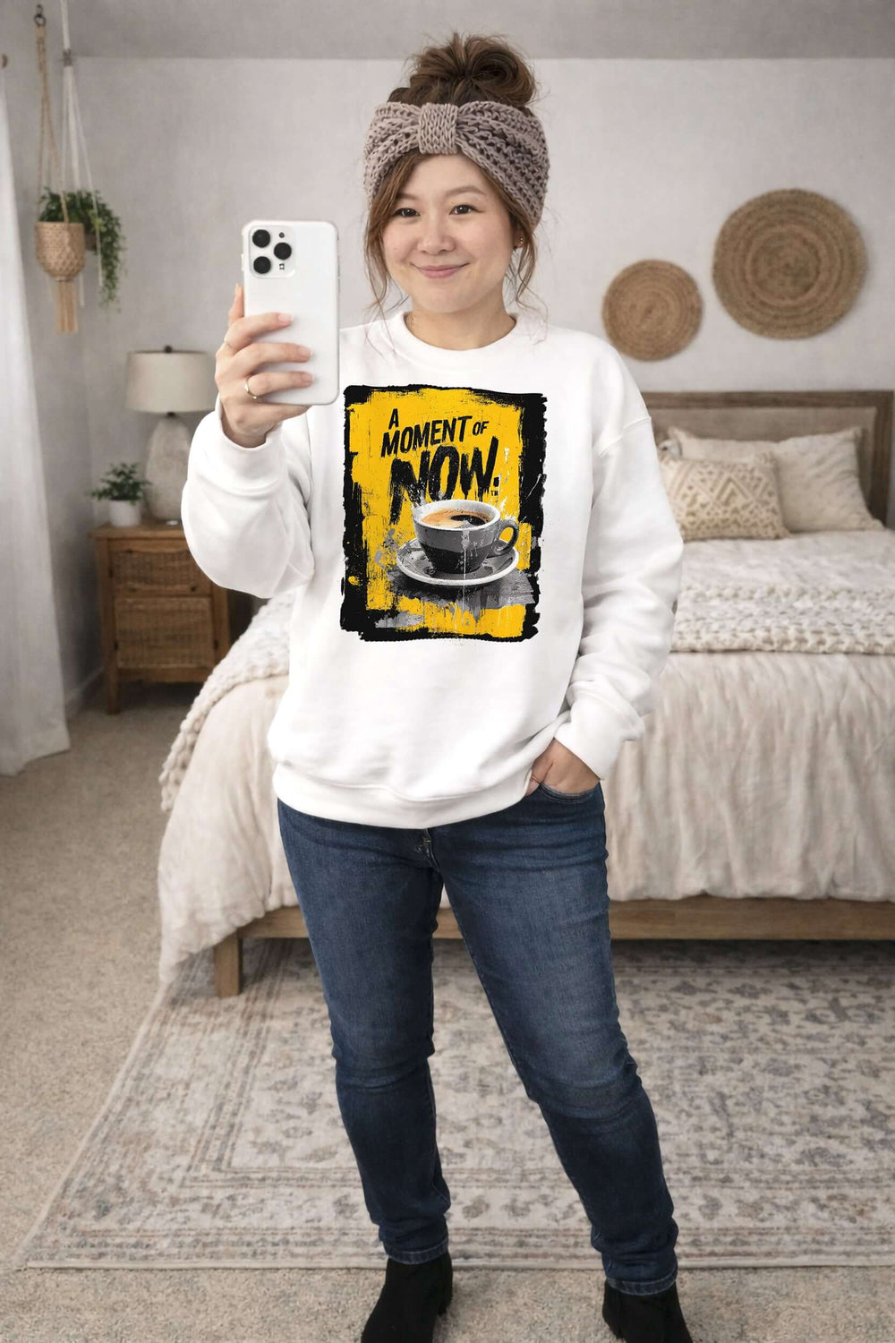 Person wearing a white sweatshirt with a coffee graphic and text, standing in a bedroom.