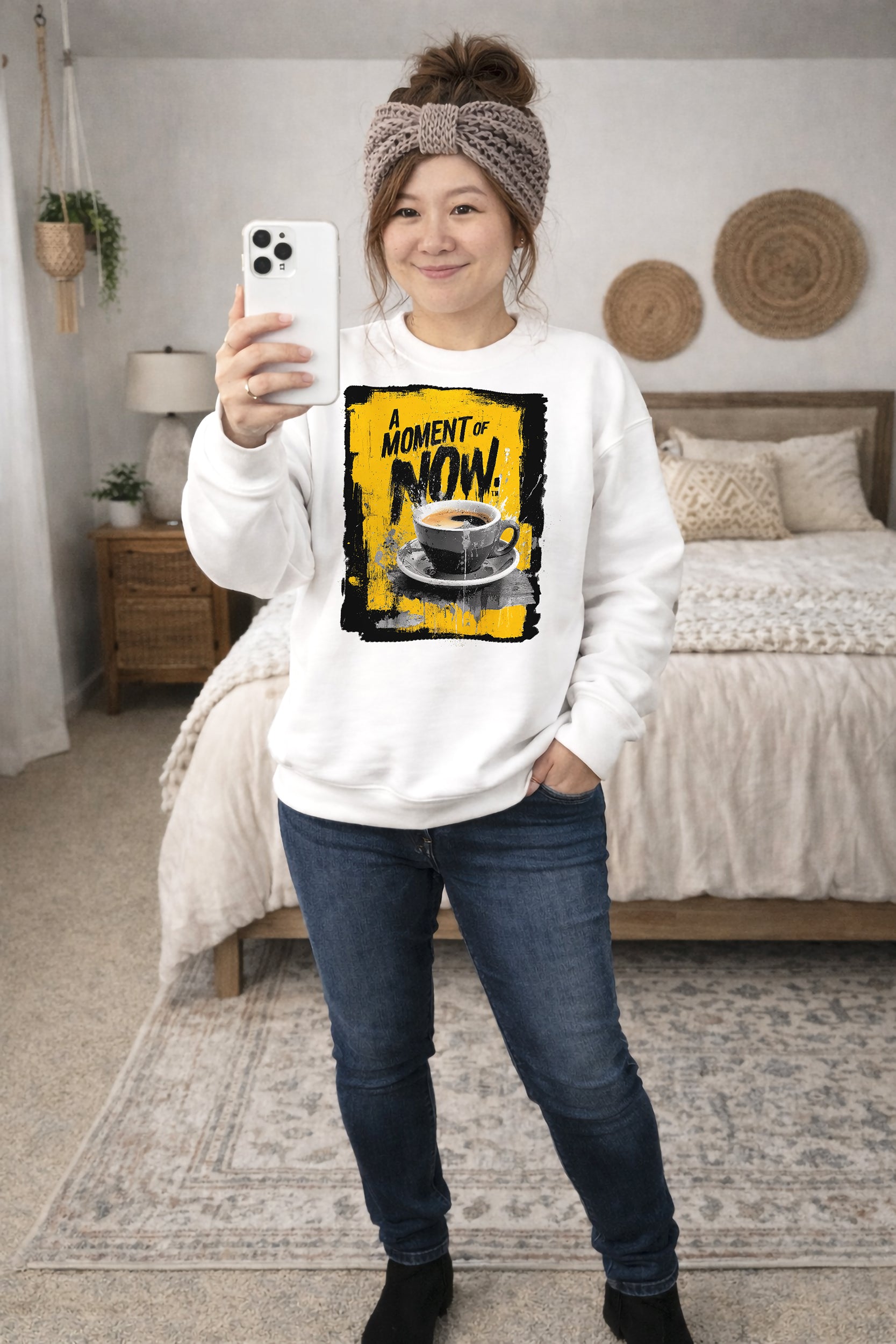 Person wearing a white sweatshirt with a coffee graphic and text, standing in a bedroom.