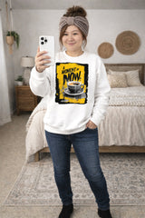 Person wearing a white sweatshirt with a coffee graphic and text, standing in a bedroom.